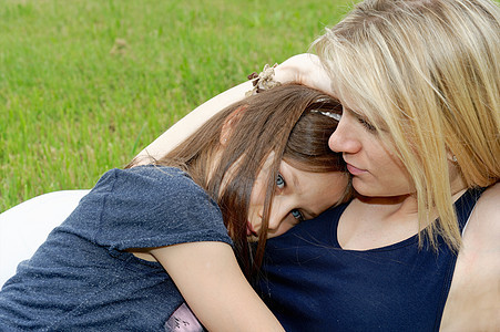 在草地坐着拥抱女孩的母亲图片