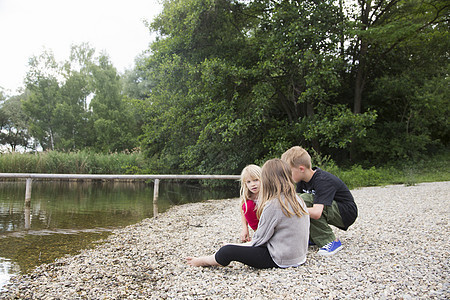 男孩和两个姐妹坐在湖边聊天图片