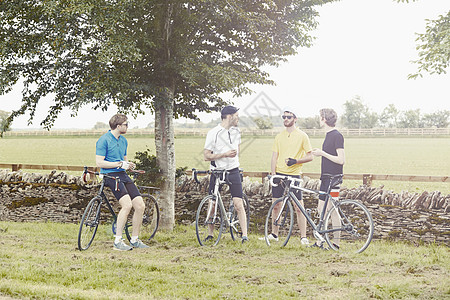 石墙旁站立的自行车运动员在聊天图片