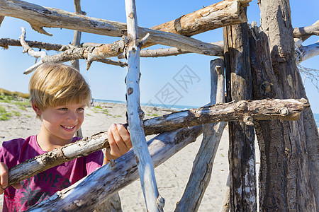 海滩上拿着浮木建造庇护所的男孩图片