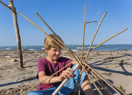 男孩在海滩上拿着浮木建造圆形结构图片