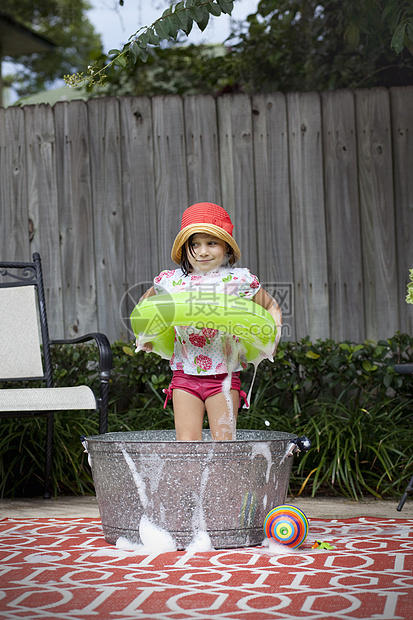 在花园的浴盆中抱着橡皮环站立的女孩肖像图片
