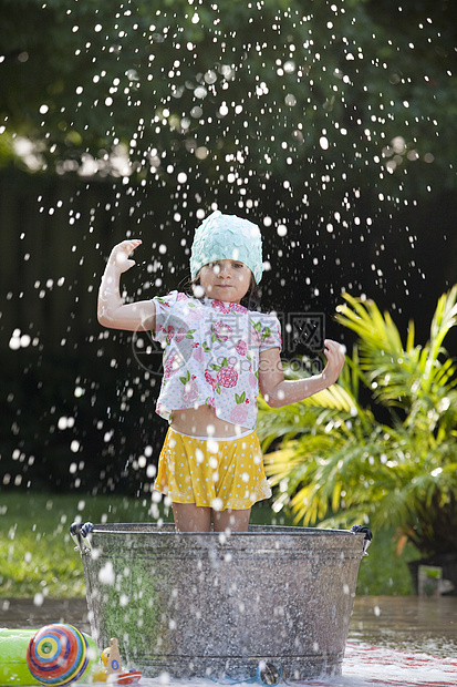 女孩站在花园的浴盆中玩肥皂泡图片