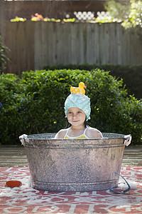 在花园的浴盆中头上戴橡胶鸭的女孩肖像图片