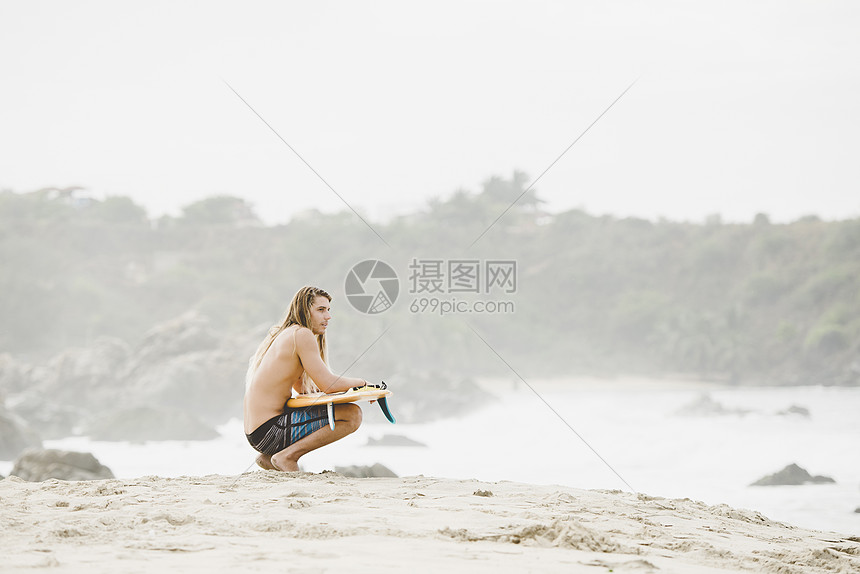 坐在海边拿着冲浪板的男人图片