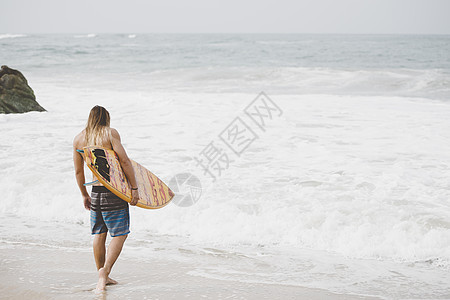 拿着冲浪板走在海滩边的男人图片