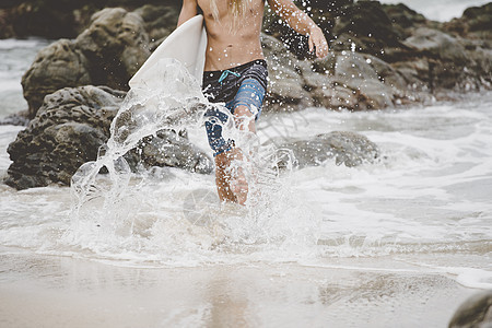 拿着冲浪板走在水里的男人图片