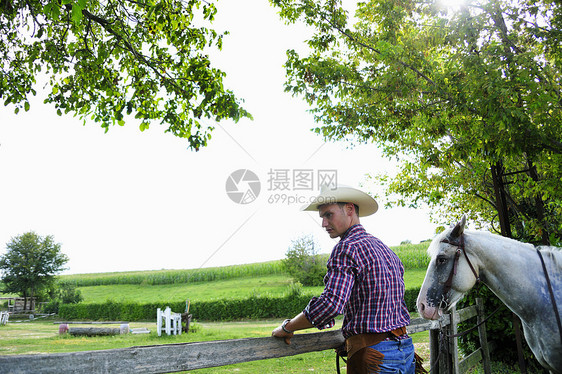 穿牛仔装的年轻男子骑马检查栅栏图片