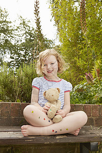 坐在花园椅子上的女孩肖像上面有泰迪熊和明星贴纸的腿图片