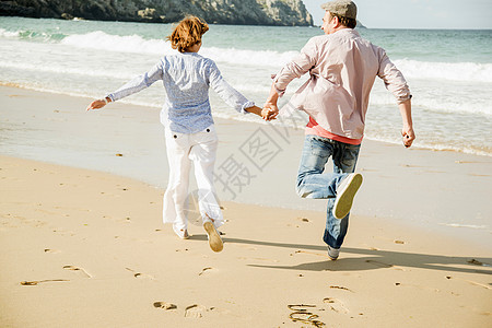 在海滩上手牵手奔跑的成熟夫妇图片