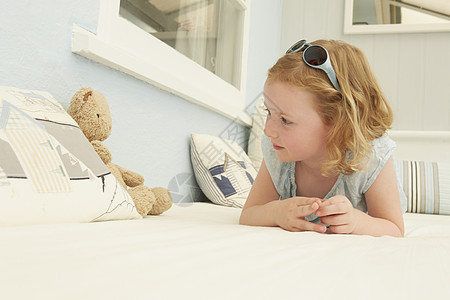 女孩与泰迪熊坐在假日公寓床上对视的肖像图片