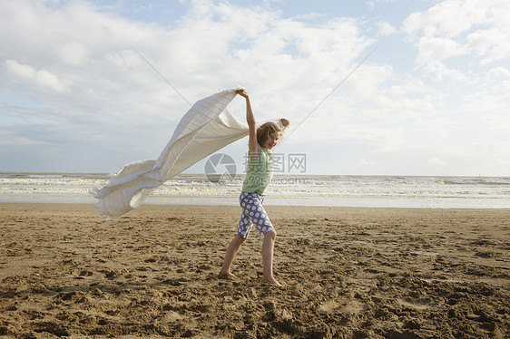 微风习习的海滩上一个女孩拿着毯子走图片