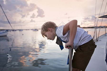 男孩在帆船上望着日落时的海下图片