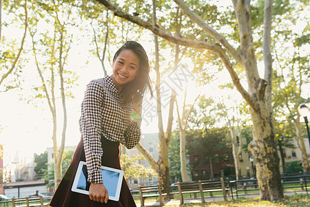 微笑的成年中女子在城市公园携带数字石板的肖像图片