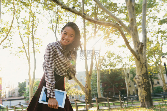 微笑的成年中女子在城市公园携带数字石板的肖像图片