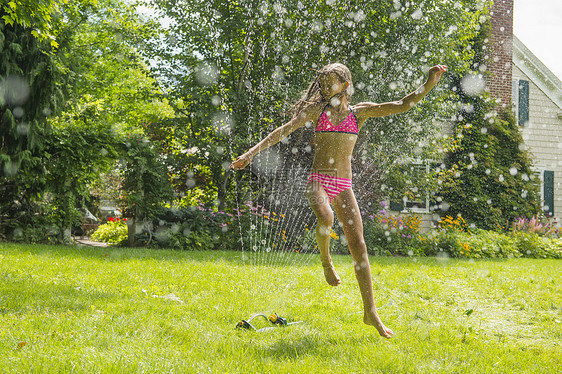 穿着泳装的女孩跳过花园喷洒器图片