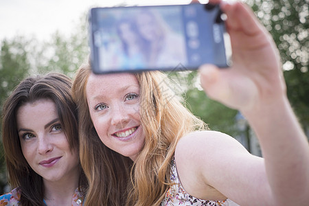 公园里两个年轻女朋友的近亲在智能手机上自拍图片