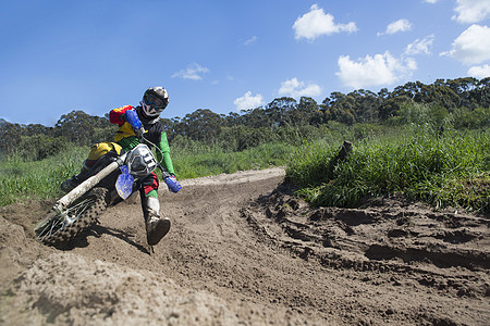 年轻的男骑摩托车手通过泥道弯曲赛车图片