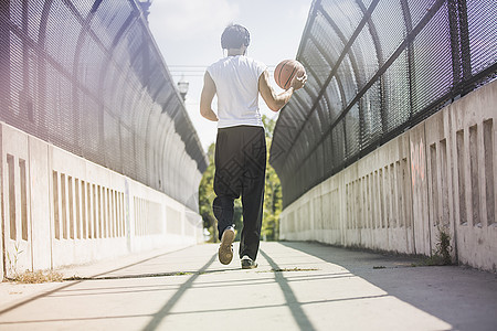 年轻男篮球运动员在步行桥上走时携带球的近视图片