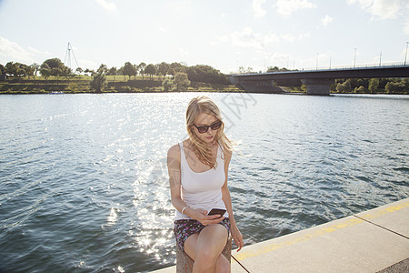 坐在河岸边的年轻女人在看手机图片