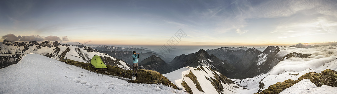在雪山顶使用智能手机拍照的成年男性图片