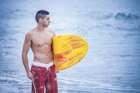 海滩上携带冲浪板的年轻男子图片