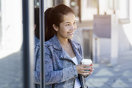 靠着公园大楼喝咖啡的年轻女子图片