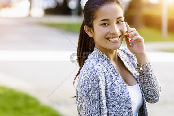 在公园里用手机聊天的年轻女子肖像图片