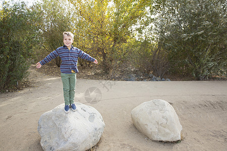 男孩站在公园的巨石上的肖像图片
