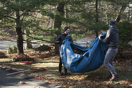 两名男园丁在公园里拿着装满秋叶的油布图片