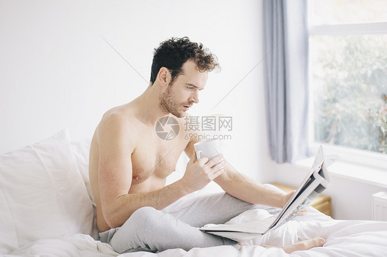 躺在床上喝咖啡阅读报纸的年轻人图片