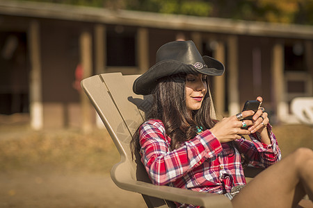 牛仔女郎在牧场的椅子上玩手机图片