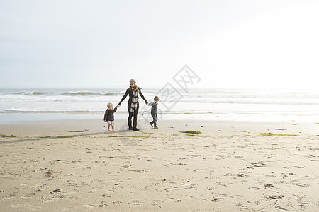 母亲牵着两个儿子的手在海滩上漫步图片