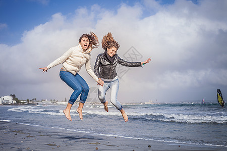 两个年轻女人手牵手在海滩跳跃图片