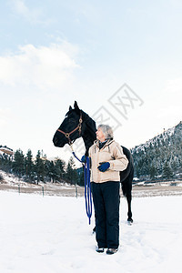 在雪地中与马站在一起的老年妇女图片