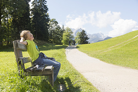 在德国巴伐利亚农村路边的公园长椅上坐着的男孩图片