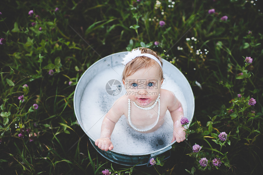 在野生花草地的锡浴缸里洗澡女婴图片