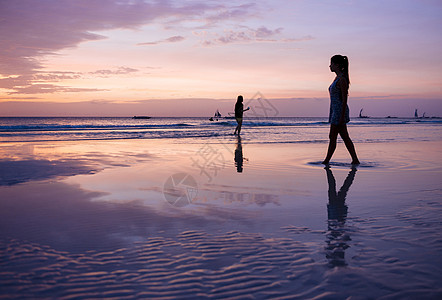 日落时在海滩上漫步的女性图片