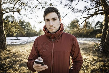 在森林湖边拿着手机的年轻男子图片