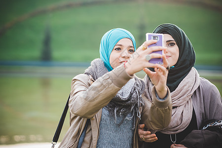 湖边两个女朋友使用智能手机自拍图片