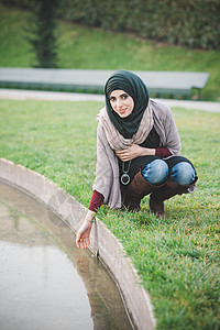 身戴头巾的年轻女子在公园湖中蹲卧的肖像图片