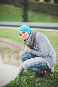 身戴头巾的年轻女子在公园湖旁边蹲卧的肖像图片