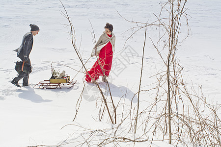女人拉着雪橇和男人走在雪地上图片