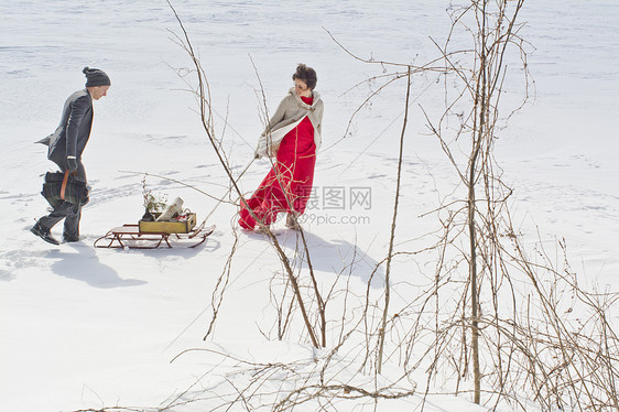 女人拉着雪橇和男人走在雪地上图片