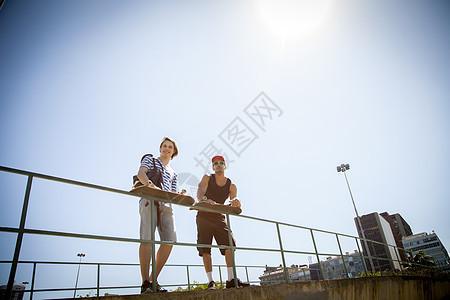 两个男人拿着滑板靠在栏杆上远望图片