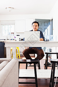 坐在厨房桌上的男子用笔记本电脑打字图片