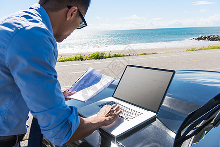 海边青年商人一边阅读文书一边用电脑打字图片