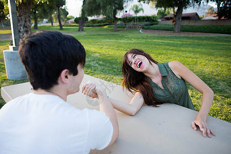 在公园野餐桌上掰手腕的年轻夫妇图片