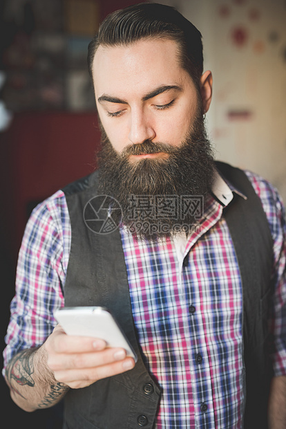 在房间里使用智能手机的长胡子年轻人图片