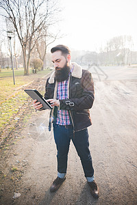 长胡子的年轻人在公园使用平板电脑图片